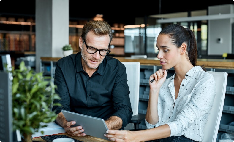Two employees in a modern office analyzing reports on a tablet.