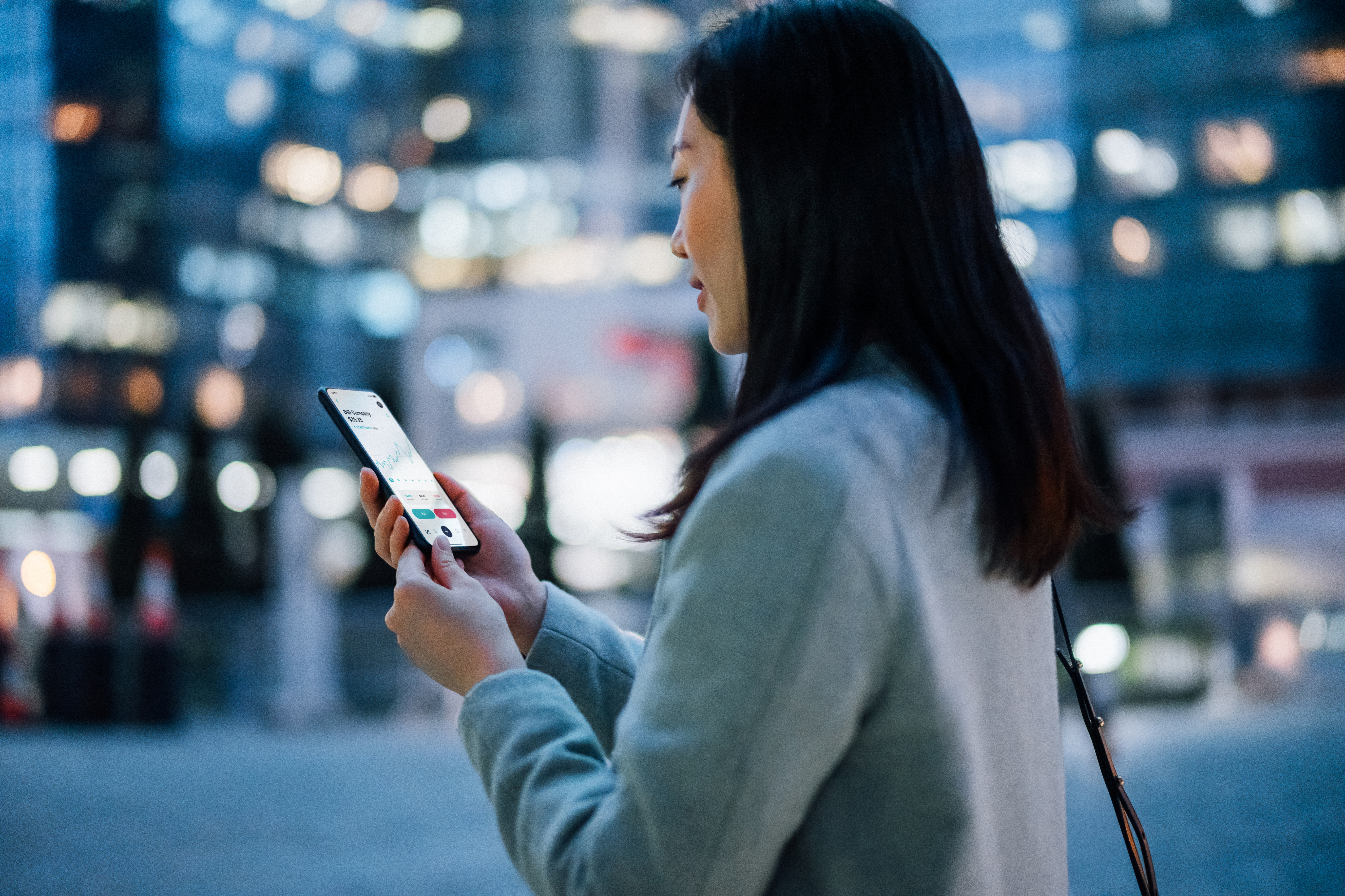 Asian woman in downtown core reading a stock chart on her phone.