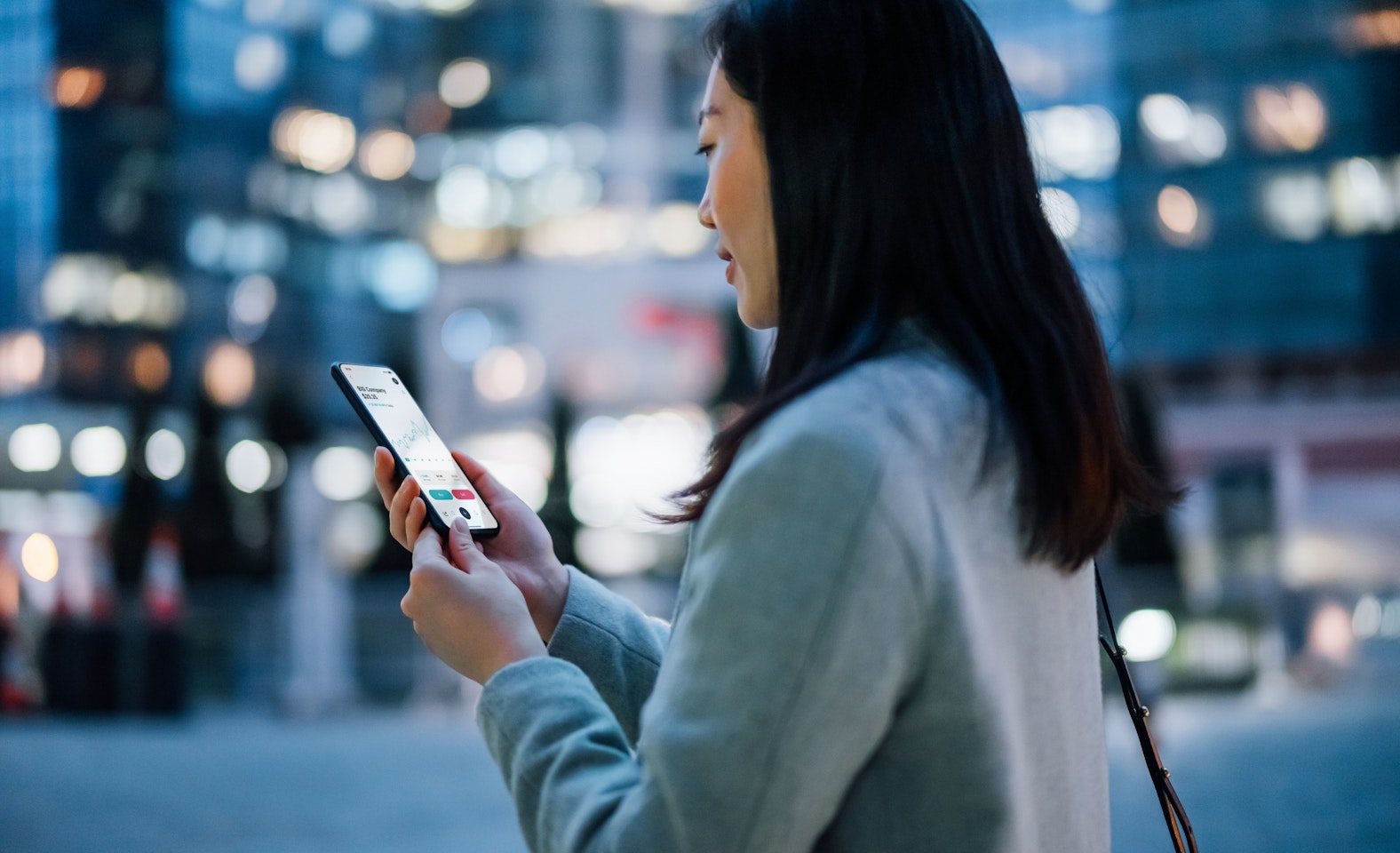 Asian woman in downtown core reading a stock chart on her phone.